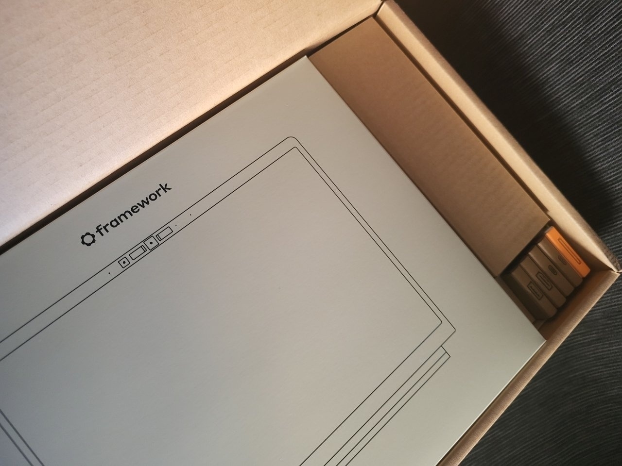 A cardboard box contains a Framework laptop packaging with a minimalistic design and visible compartments on the side.